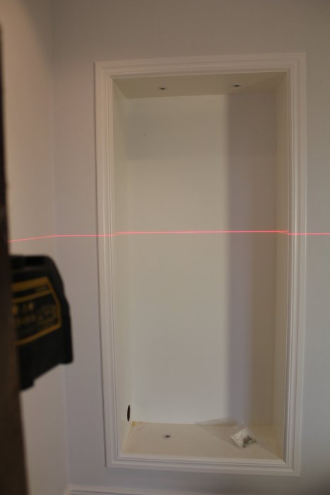 En öppen vit väggnisch redo för installation med laser-nivelleringsverktyg som projicerar en röd linje.