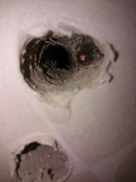 Hål i lättbetongvägg med synligt rör och skada från borrmaskin, misstänkt kopparledning.