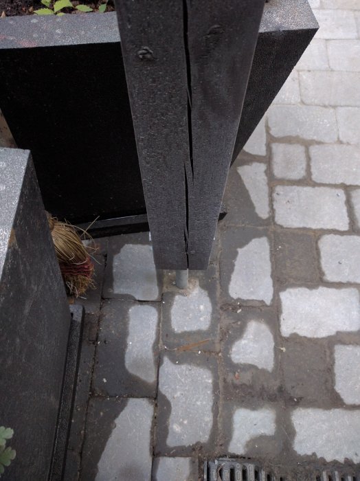 Ett svartmålat stolpe med en synlig balksko fäst vid en stenbelagd mark.