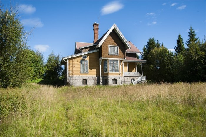 Eklektisk stilhus i två våningar med veranda, omringat av grönt landskap och högt gräs.