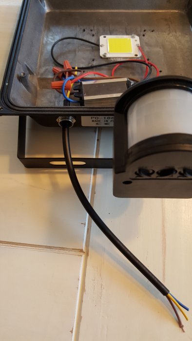 LED strålkastare öppnad, internt kablage synligt med okopplad jordkabel, CE-märkning på baksidan.