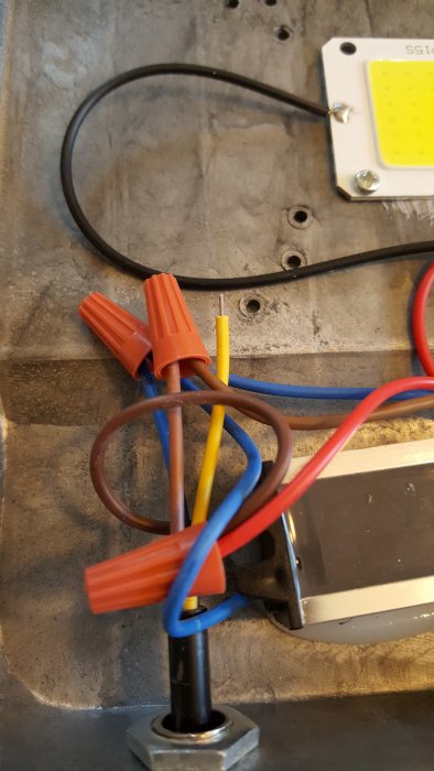 Öppen LED strålkastare med okopplad gul jordkabel och andra kablar bundna med skarvdon.