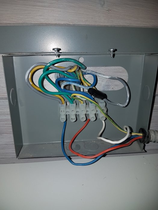 Kopplingsdosa med färgkodade elkablar anslutna till klemrader, inklusive en oidentifierad gul kabel.