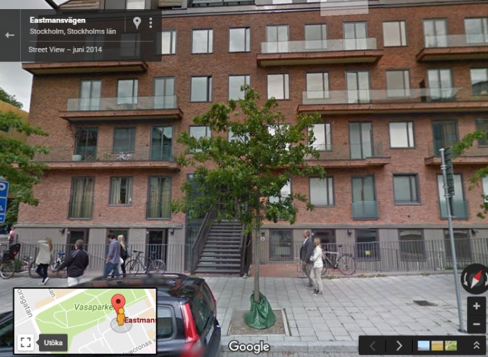 Street View-bild av tegelbyggnad med flerbostadshus, människor och cyklar på gatan.