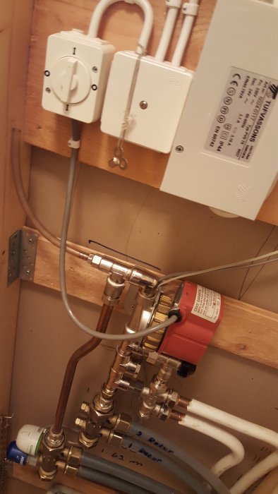 Värmesystemskåp med Wirsbo kontrollenheter, ledningar och en röd cirkulationspump.