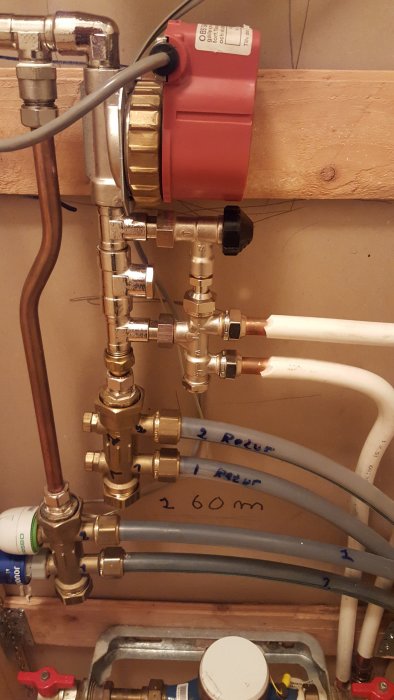 Värmesystem med kopparledningar, ventiler och en röd cirkulationspump monterad på en träbjälke.