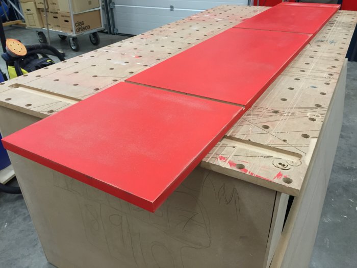 Rödmålad träyta som är våtslipad ligger på arbetsbänk i verkstad.