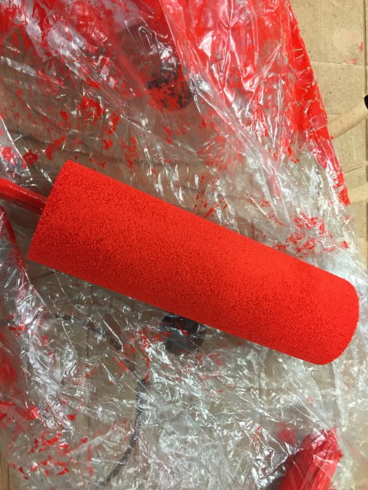 Ny roller för målning med röd färg på plastöverdraget skyddsunderlag.