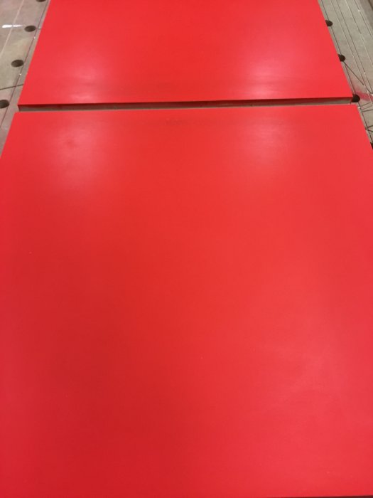 Träpanel målad i matt röd färg ligger på ett träunderlag i verkstadsmiljö.