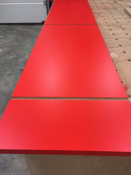 Rödmålade och slipade träytor på en arbetsbänk, troligen under förberedelse för lackering.