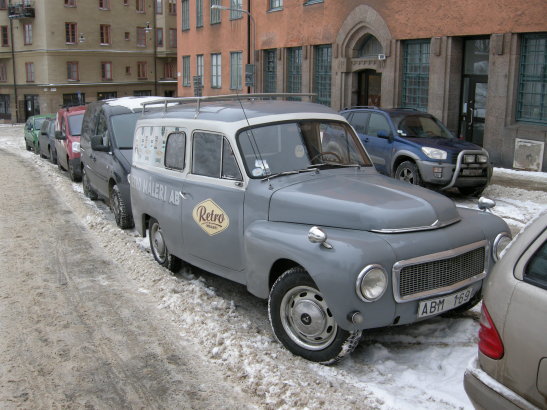 Grå Volvo Duett med "Retro" logotyp parkerad på snötäckt gata i urban miljö.