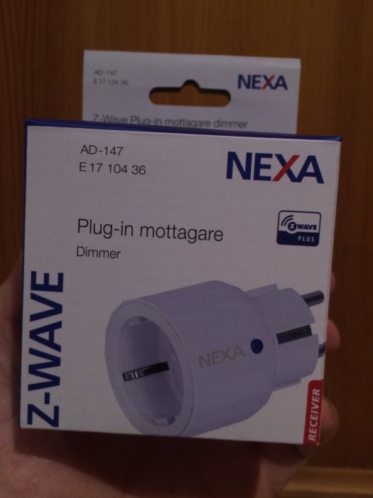 Hand håller en NEXA Z-Wave plug-in mottagare dimmer i dess förpackning.