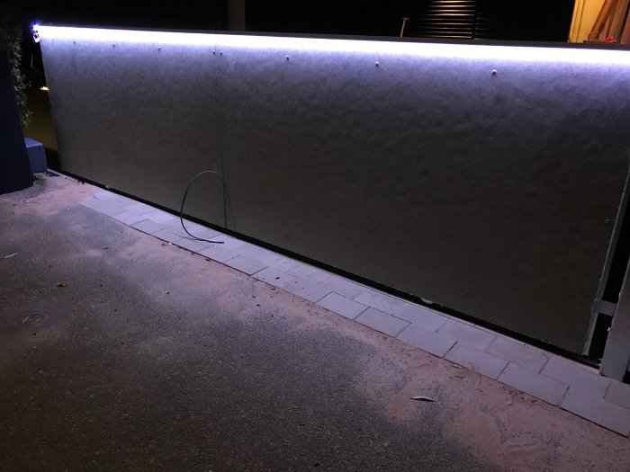 Monterad aluminiumlist med LED-profil som lyser upp på en vägg utomhus under skymning.