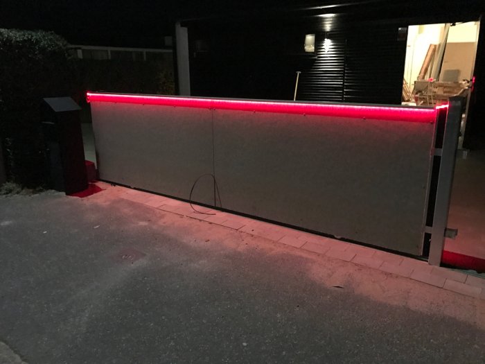 Aluminiumlister med röd LED-belysning monterade längs en uteplats staketkant i mörker.