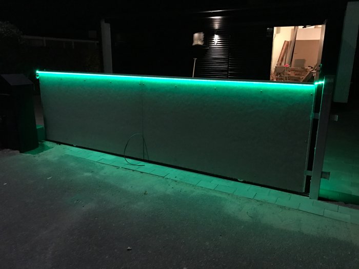 Vägg utomhus med grönt LED-ljus från monterade aluminiumlister vid kvällstid.