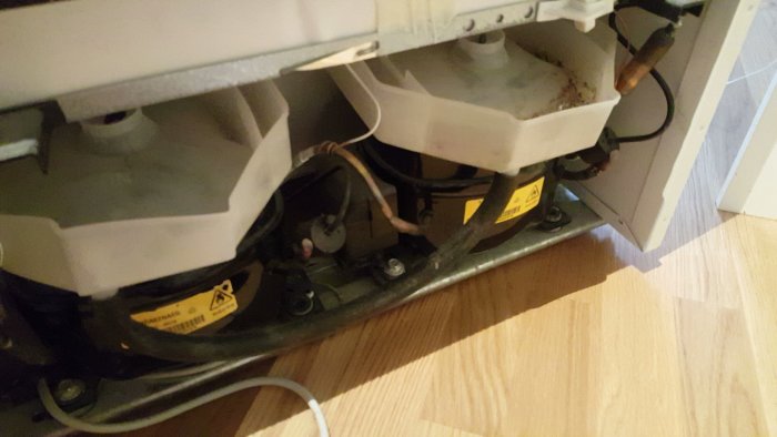 Bakre delen av en frys med synlig höger kompressor och ledningar.