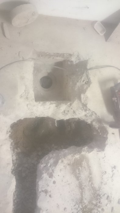 Nygrävd grop i betonggolv visar gammalt vattenrör och grundvattenstånd.