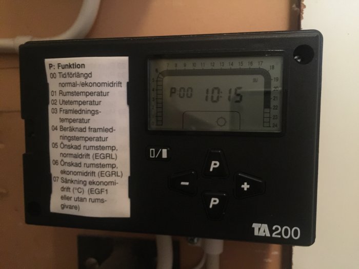 En TAC200 styrenhet med en LCD-display som visar tid och menyalternativ för värmesystemets funktioner.