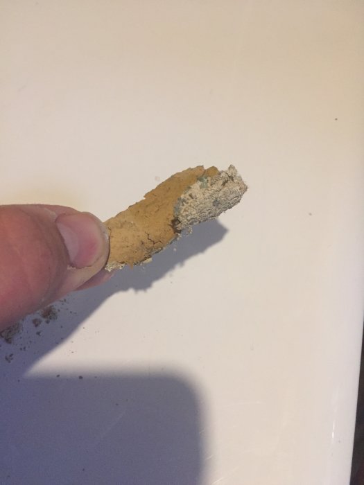 Hand håller en flaga av gammal färg som lossnat från en källarvägg.