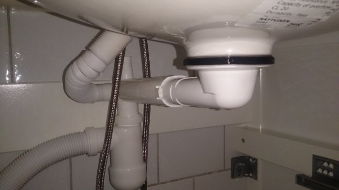 Avlopp med vit plaströrskoppling och svart tätning under diskbänk, lätt läckage synligt.