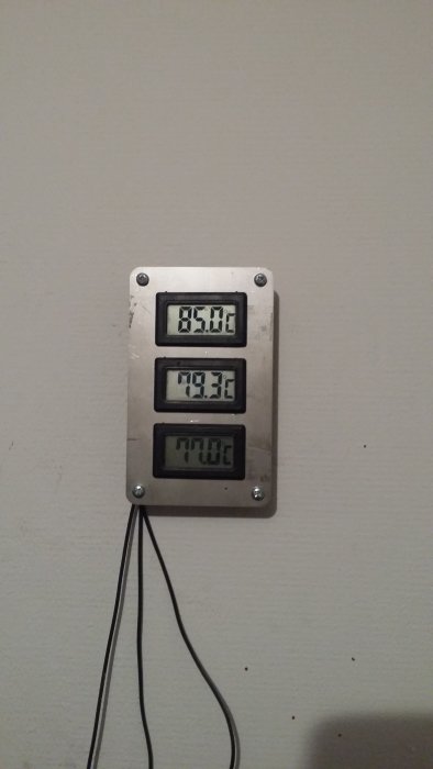 Digital värmeregulator på vägg visar tre olika temperaturer.