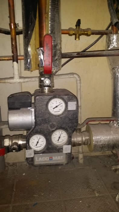 Laddomatpump med mätare och rör i en teknisk installation, täckt av smuts och damm.