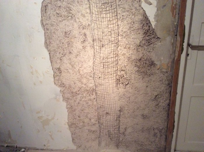 Vägg i källare med gammal puts och synlig Träullit samt överlagt armeringsnät.