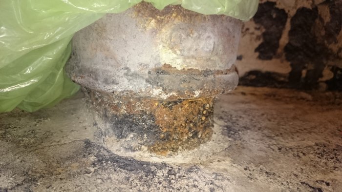 Rostigt avloppsrör i betonggolv med synliga skador, omgivet av borttaget klinkers.