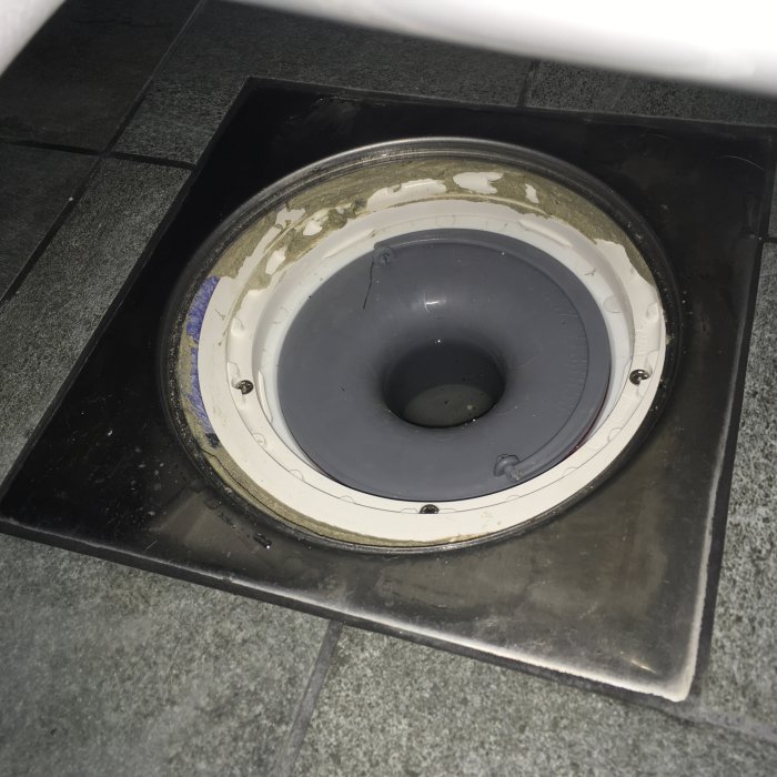 Renoverat badrum med golvbrunn där metallramen inte är centrerad och tätskikt är synligt.