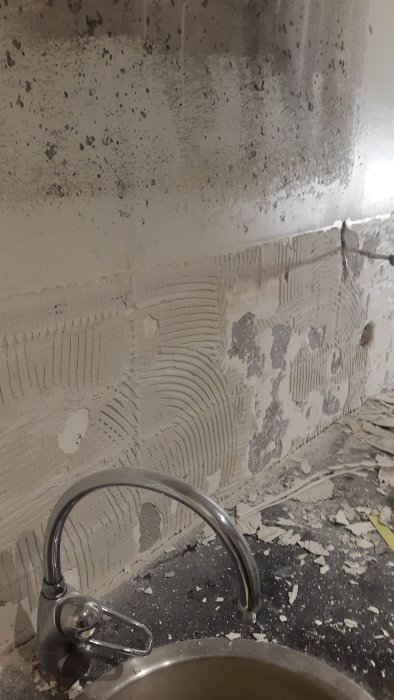 Renoveringsarbete i kök med synligt fix och rester på betongvägg och kakelspill på bänk.