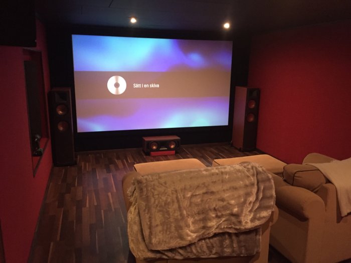 Hemmabiorum med röda väggar, 120" filmduk och 7.2 Klipsch ljudsystem, mysiga soffor och en filt.