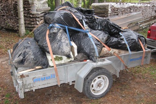 Släpvagn fylld med svarta sopsäckar innehållande insamlat plastskräp och trä från stränder.