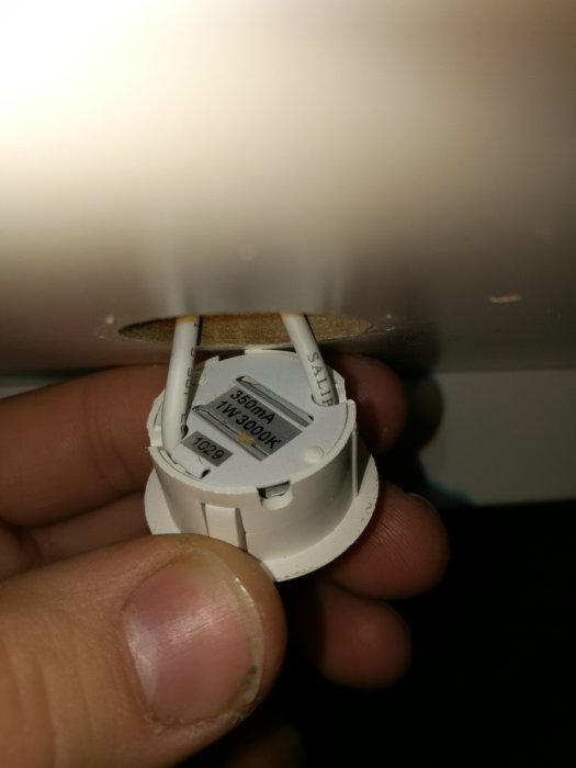 Hand håller en takspot med etikett och specifikationer synliga under montering.