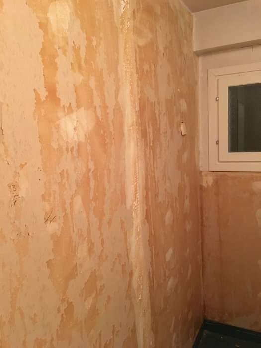 Delvis riven tapet i ett badrum under renovering med synliga väggstrukturer.