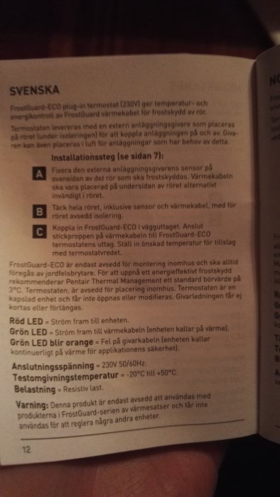 Hand som håller ett öppnat bruksanvisningshäfte för FrostGuard-ECO termostat med installationsinstruktioner på svenska.