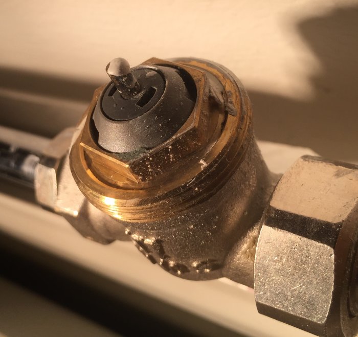 Närbild av en radiatorventil som kan vara strypt, med damm och synliga justeringsdetaljer.