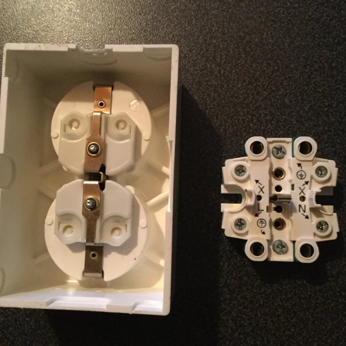 Elektrisk dosa med öppen front och bakhållet kontaktstycke bredvid, avsedd för väggmontering.