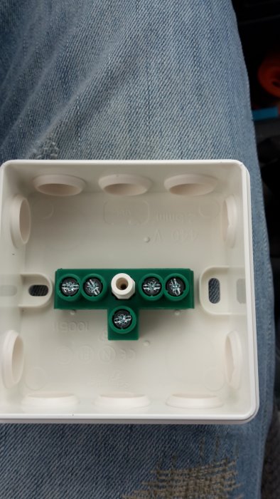Öppen vit anslutningsdosa i någons knä med grön kabelklämma och skruvkontakter redo för installation.