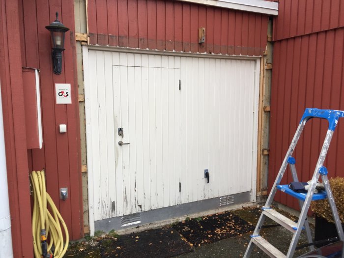 Stängd garageport före renovering med en stege till höger och gula slangar till vänster.