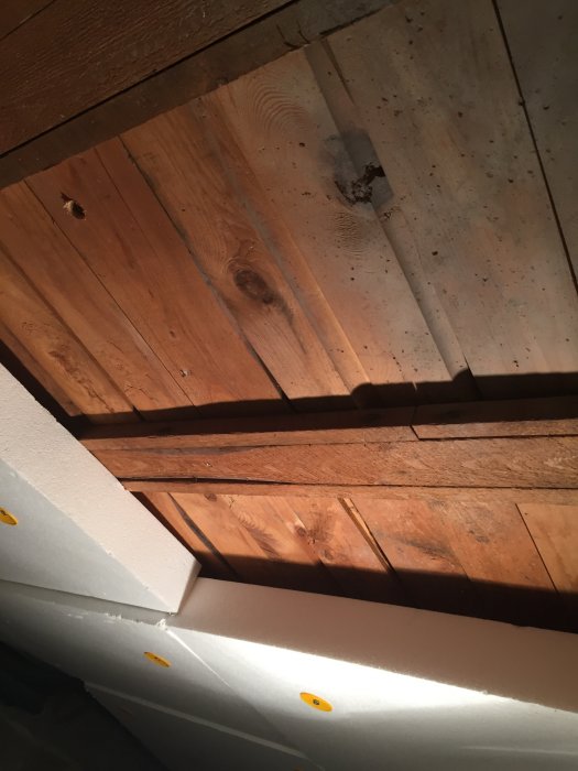 Vy av ett öppet bjälklag med träbjälkar och frigolitisolering längs kanterna i ett hus.