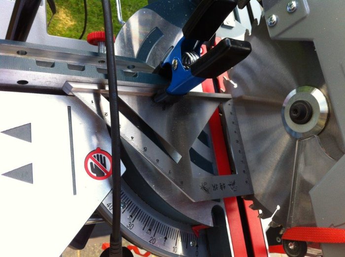 En vinkelhake kläms fast mot anhållet vid justering av en geringssåg.