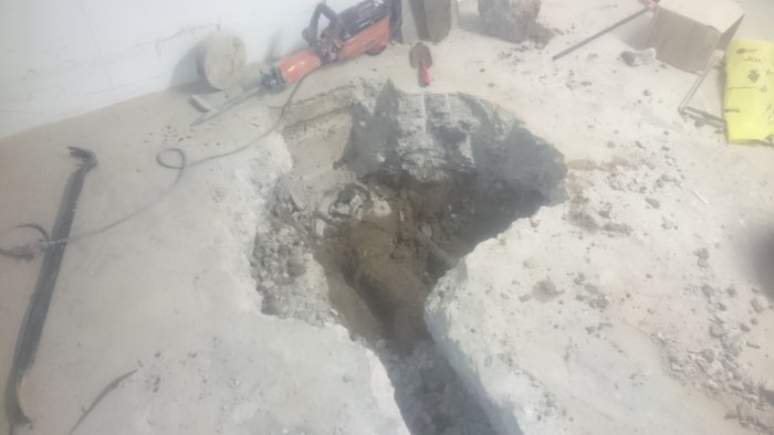 Grävt hål i betonggolv för installation av durkplåtslucka och backventil, verktyg syns.