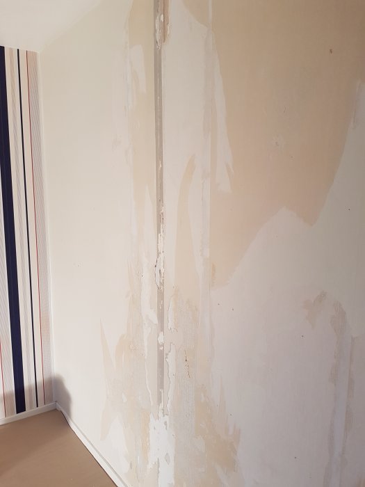 Vägg med avflagning av spackel och färg, där betong möter annat material i en inomhusmiljö.
