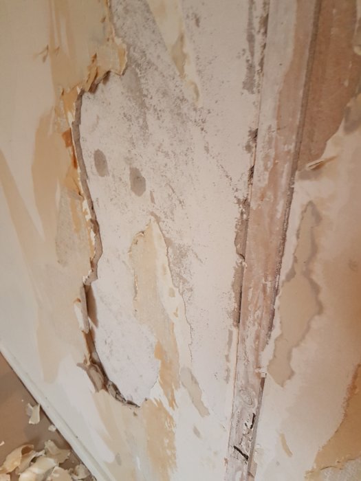 Vägg med flagande lager av okänt material som avslöjar underliggande betongstruktur.