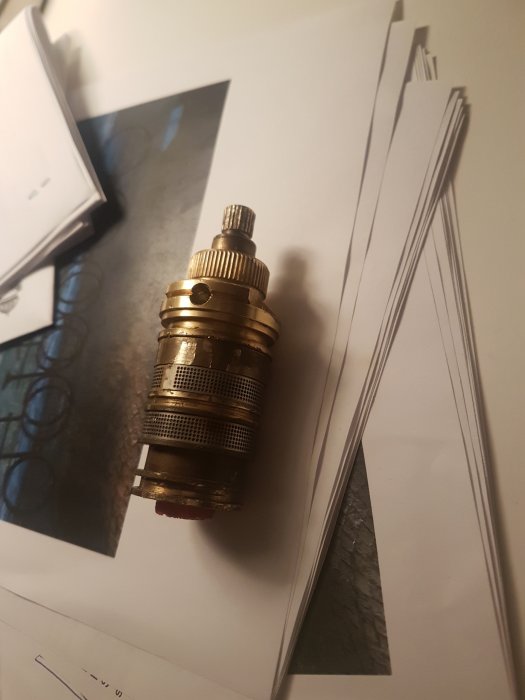 En termostatventil för radiator ligger på ett bord med dokument och ritningar i bakgrunden.