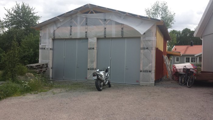 Halvfärdigt garage med pågående byggnadsarbete, taköverhäng och parkerad motorcykel.