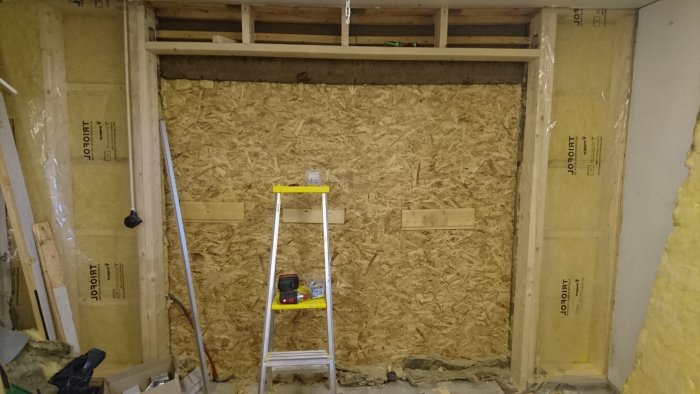 Garage under renovering med nya reglar, isolering, OSB-skivor på väggen, samt en stege i mitten.