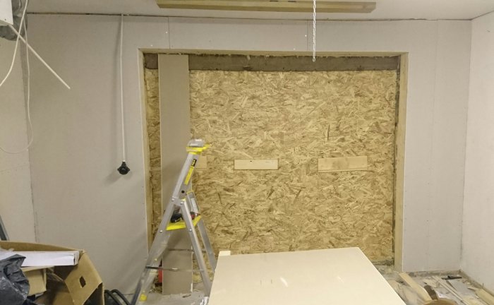 Inre garagevägg med OSB-panel, gipsskivor och grundfärg, stegar och byggmaterial synliga.