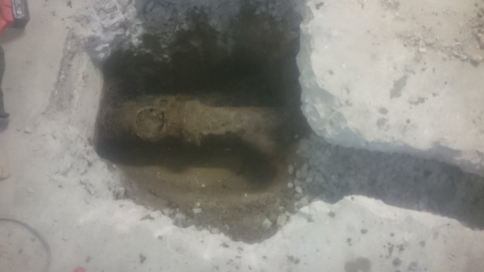 Djup grop i betonggolv med grus och lerlager, förberedd för installation av ventil och gjutning.