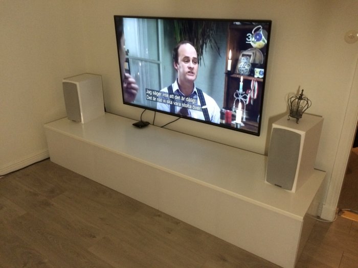 Hembyggd vit bänk med dimensioner 2440x400x600mm under en TV, flankerad av högtalare, utan luckor.